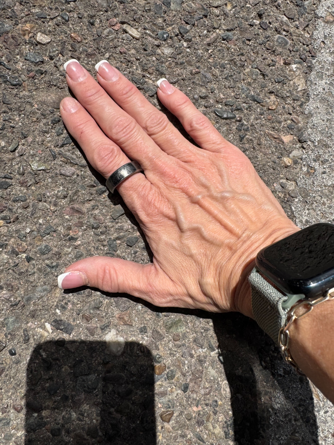 Gina's hand flat on the concrete parking lot, Apple Watch on her wrist showing the timer — the seven-second pavement test in progress.